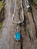 Sterling silver long drop pendant with sky blue agate rose cut oblong flower and silver snake chain. sitting on a mossy log in the sunshine